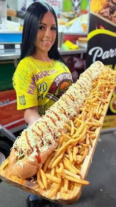 a woman holding a large hot dog and french fries