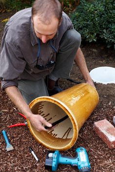 a man kneeling down next to a bucket with tools on the ground in front of him