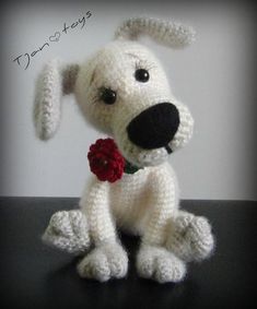 a crocheted white dog with a red rose in its mouth sitting on a table