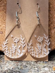 a pair of earrings with flowers and leaves etched on the outside of them, sitting on a piece of cardboard