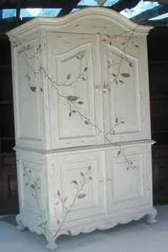 an old white armoire with vines painted on the front and sides, sitting in a room