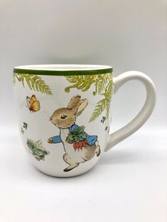 a white coffee cup with an image of a rabbit on it's side and green trim around the edge