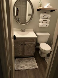 a white toilet sitting next to a bathroom sink under a round mirror on top of a wooden cabinet