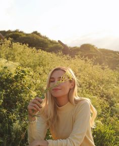 a woman is sitting in the grass with her eyes closed and looking up at something