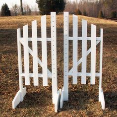 a white picket fence sitting in the middle of a field with trees and grass behind it