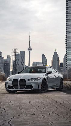 a silver sports car parked in front of a large city with tall buildings behind it