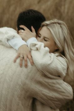 a man and woman hugging each other in the middle of a field with brown grass