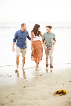 three people walking on the beach holding hands and looking at each other with an ocean in the background