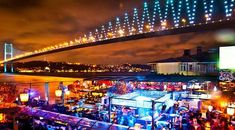 a group of people standing around in front of a bridge at night with lights on