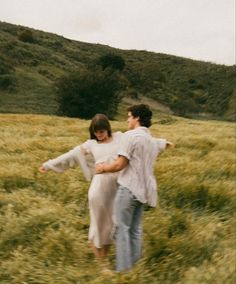 a man and woman walking through a field holding each other's arms as if they were in love