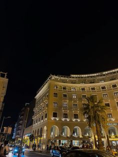 cars are parked on the street in front of a large building at night with palm trees