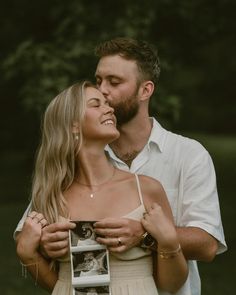 a man and woman standing next to each other in front of some trees with their heads close together