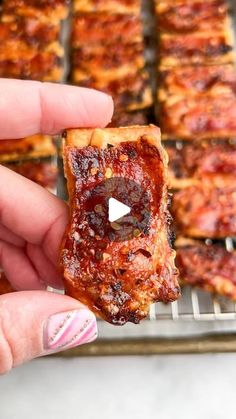 a person holding up a piece of pizza in front of some other food on a rack