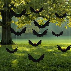 many bats are hanging from the branches of a tree in a field with green grass