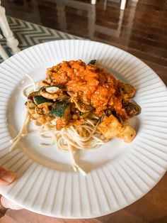 someone is holding up a plate of pasta with sauce and spinach on the side