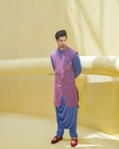 a man standing in front of a yellow wall wearing a pink and blue outfit with red shoes