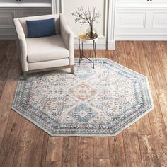 a living room area with a chair and rug on the wooden floor, in front of a white paneled wall