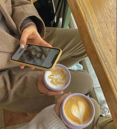 a person holding a cell phone and two cups of coffee