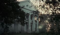 an old white house with columns and trees in the foreground