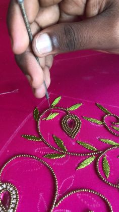 someone is working on an embroidered design with scissors and thread in their hands, while another hand holds a needle