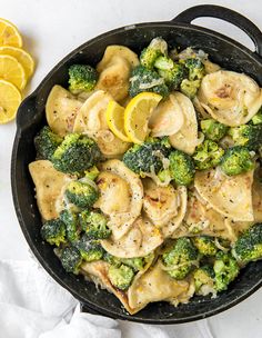 a skillet filled with chicken and broccoli covered in sauce next to sliced lemons