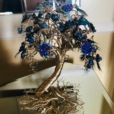 a metal tree with blue glass beads on it's branches and roots in front of a mirror