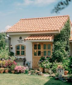 a small white house with lots of flowers and plants around it's front door