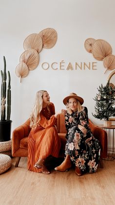 two women sitting on chairs in front of a wall with oceanine written on it