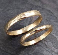 two gold wedding rings sitting on top of a stone slab, with one ring in the middle