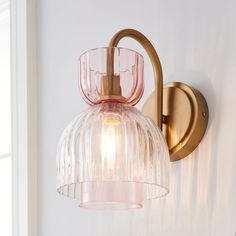 a pink glass light fixture mounted on a white wall next to a window in a room