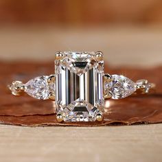 an emerald cut diamond ring with three pear shaped diamonds on the band and side stones