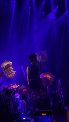 two people standing in the middle of a stage with purple lights behind them and flowers on the floor