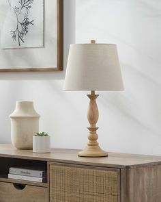 a table with a lamp on it next to a vase and a framed picture in the background