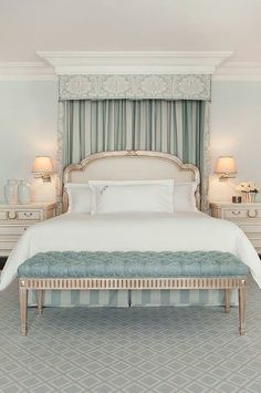 a large white bed sitting in a bedroom next to two night stands and lamps on either side of the bed