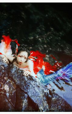 a woman laying on top of a rock next to water