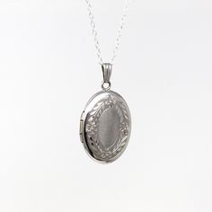 Beautiful estate circa 2000's era 14k white gold photo locket! This lovely oval pendant has a floral leafy border on the front. The keepsake locket is shown modeled on a brand new sterling silver 20" chain. A classic piece of fine keepsake jewelry!  ERA - Circa 2000's - Estate METAL / MATERIAL - 14k white gold locket, sterling silver chain    MARKINGS / HISTORY - Back of locket is marked "14k" with a letter "M" in a diamond shape for Marathon CONDITION - Good condition. White gold metal has been professionally polished & cleaned. Age appropriate patina & wear remains. Amazing modern locket!  SIZE / MEASUREMENTS - Chain Modeled: 20 inches, Pendant (including bail): 1 1/8 x 1/2 inches, Weight (without chain): 2.64 grams PRESENTATION - Listing includes a complimentary MJV logo gift box, as sh Elegant Hallmarked White Gold Locket Necklace, Timeless Silver Oval Pendant Jewelry, Classic White Gold Oval Pendant Jewelry, Vintage Oval Sterling Silver Locket Necklace, Vintage Sterling Silver Oval Locket Necklace, Timeless Engraved Oval Pendant Jewelry, Classic Engraved White Gold Locket Necklace, Hallmarked Oval Pendant Jewelry For Keepsake, Elegant White Gold Round Pendant Locket Necklace