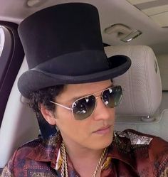 a man wearing sunglasses and a top hat in the back seat of a car,