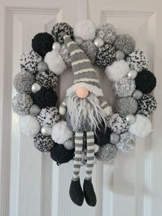 a wreath decorated with pom poms and a gnome figure hanging from the front door