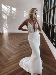 a woman in a white dress taking a selfie with her cell phone while standing on a wooden floor