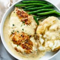 a white plate topped with chicken and mashed potatoes covered in gravy next to green beans