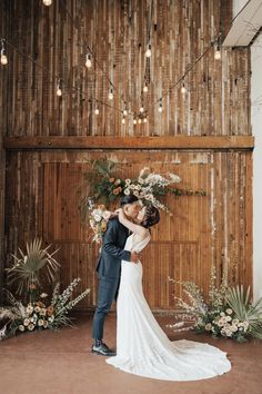 a bride and groom kissing in front of a wooden wall with hanging lights at their wedding