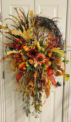 a wreath is hanging on the front door with fall foliages and leaves around it