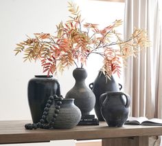 three vases are sitting on a table with a book and plant in the background