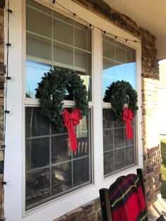 two wreaths on the windows of a house with red bows and plaid blanket hanging from them