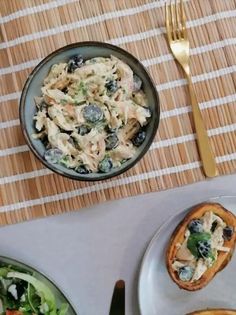 a table topped with plates of food next to a bowl of salad and bread on top of a mat