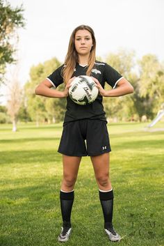 a female soccer player holding a ball in her hands and posing for the camera on a grassy field