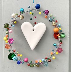 a white heart hanging on the side of a door with beads and charms around it