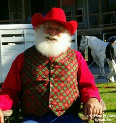 an old man wearing a red hat and vest sitting on a bench in front of horses