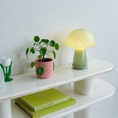 a white table topped with a green plant next to a yellow lamp and books on top of it