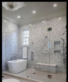 a white bathtub sitting next to a walk in shower under a chandelier